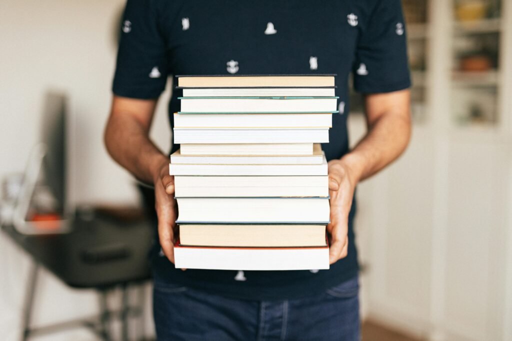 A person holding a stack of books indoors, capturing the essence of knowledge and learning.